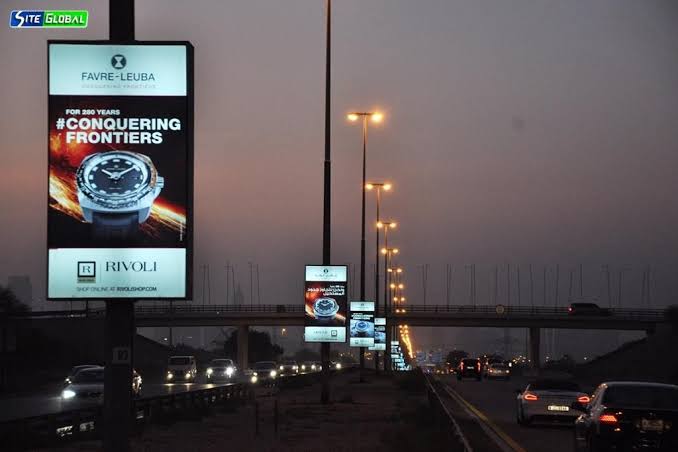 back view of woman wearing a backpack and beanie waiting to cross the road on a busy street at night in New York City, USA